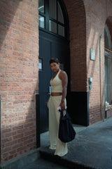 Woman in a white outfit standing against a brick wall with a black door.