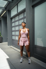 Woman in pink athletic wear standing on a sidewalk with a modern building in the background